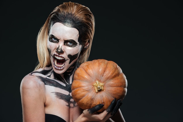 Foto vrouw met bange gotische make-up die pompoen vasthoudt en over zwarte achtergrond schreeuwt