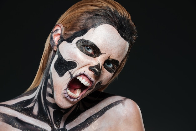 Vrouw met bange halloween-make-up en geopende mond die over zwarte bakground schreeuwt