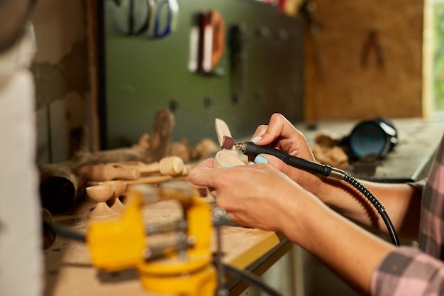 Vrouw met behulp van elektrisch gereedschap graver voor houten gebruiksvoorwerpen lepel