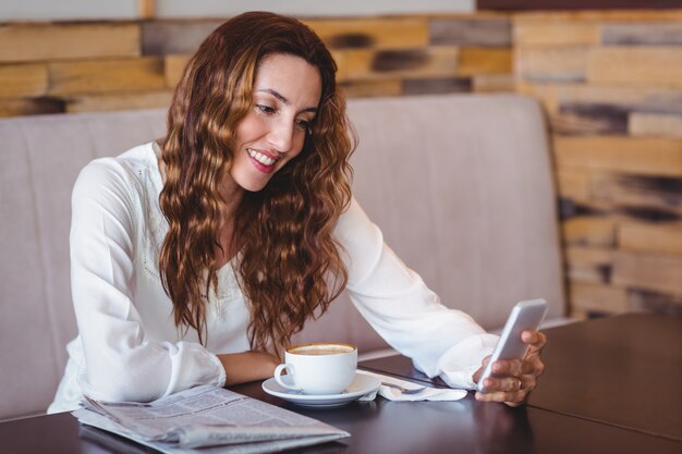 Vrouw met behulp van haar mobiele telefoon en kopje koffie te houden