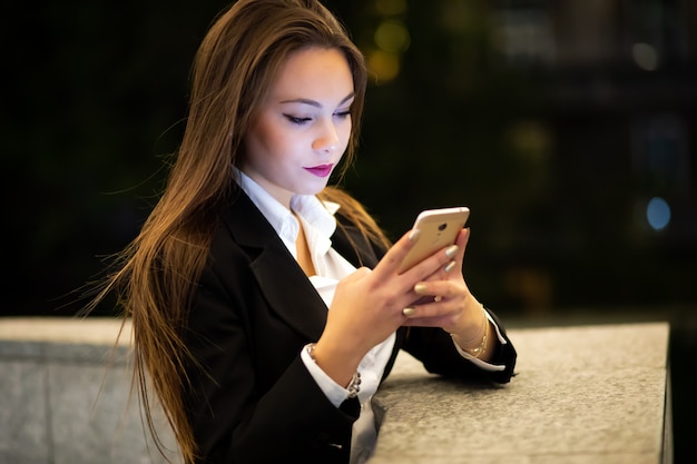 Vrouw met behulp van haar smatphone buiten in de avond in een moderne stad omgeving