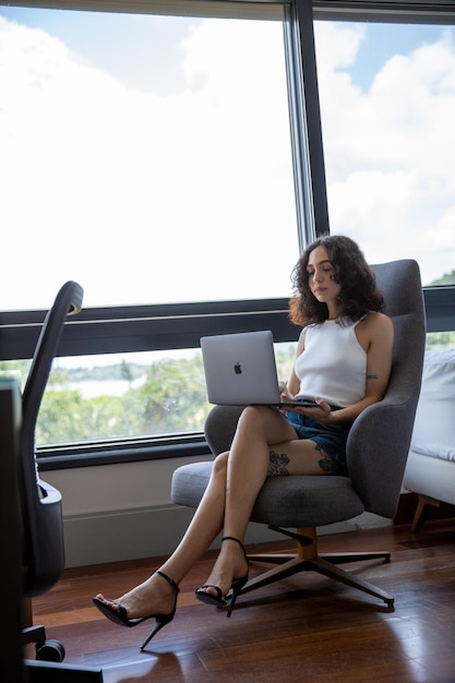 vrouw met behulp van laptop, portret van een mooie vrouw zittend in een fauteuil met haar computer, tatoeage