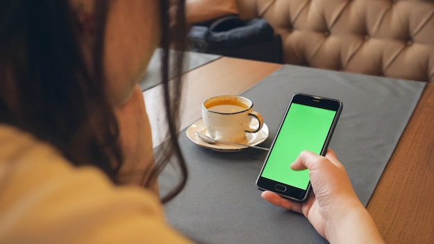 Vrouw met behulp van mobiele telefoon met groen touchscreen in café, close-up