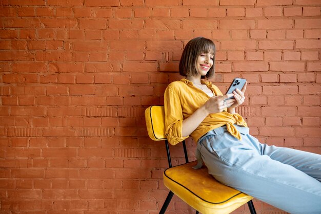 Vrouw met behulp van slimme telefoon zittend op een stoel op bakstenen muur achtergrond