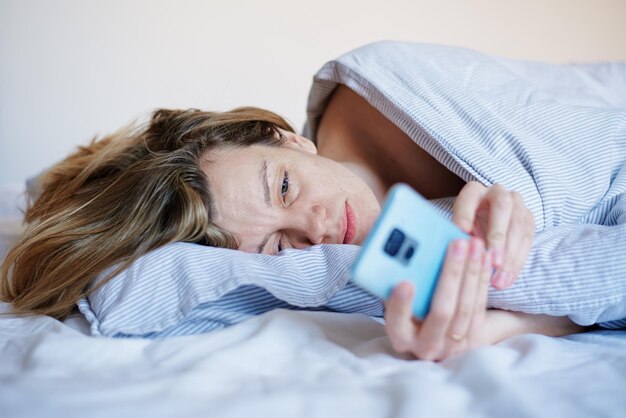 Vrouw met behulp van smartphone in het bed sociale media lui weekend