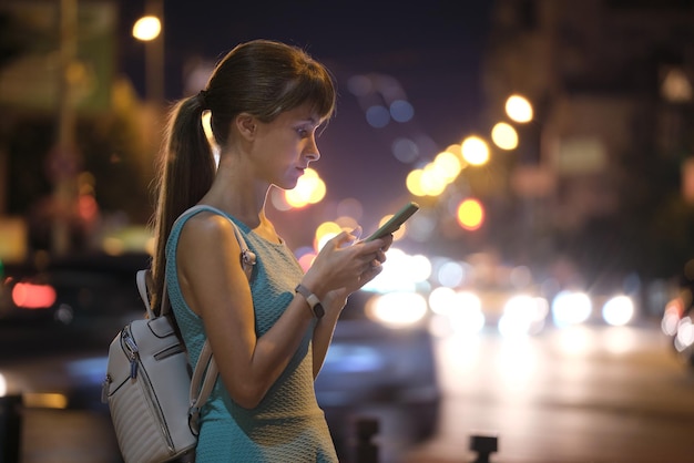 Vrouw met behulp van telefoon wijzende vinger op smartphone scherm op de achtergrond van bokeh lichten in nacht atmosferische stadsverlichting in avond intreepupil straat. Online levensstijl met internetverbinding.