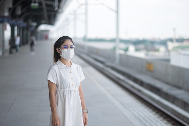 Vrouw met beschermend gezichtsmasker ter voorkoming van coronavirus en PM 2.5-vervuiling tijdens wachtende trein. openbaar vervoer. veiligheid onder covid-19 pandemie en stof