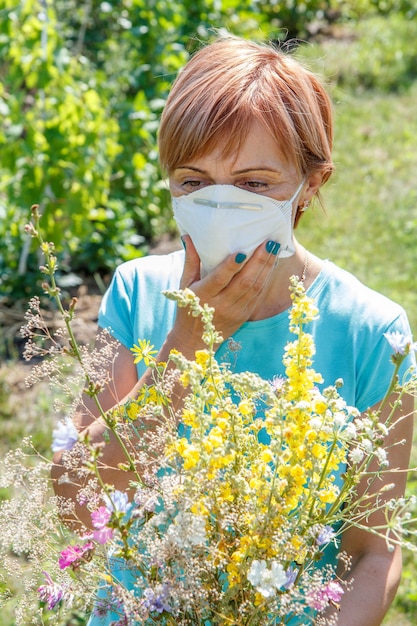 Vrouw met beschermend masker die een boeket van wilde bloemen vasthoudt en probeert allergieën voor stuifmeel te bestrijden. Natuurlijk daglicht. Allergie concept.