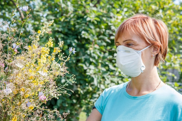 Vrouw met beschermend masker die een boeket van wilde bloemen vasthoudt en probeert allergieën voor stuifmeel te bestrijden.