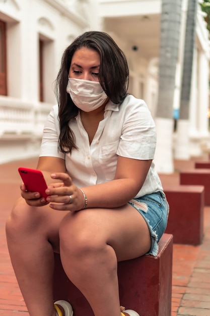 Vrouw met beschermend masker in de stad die haar mobiele telefoon controleert