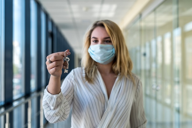 vrouw met beschermend masker met huissleutels in het moderne zakencentrum