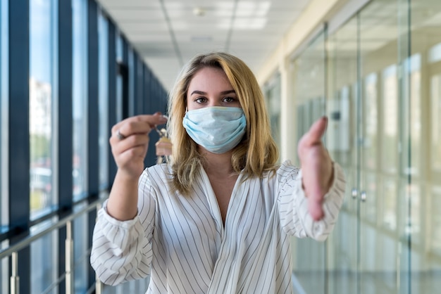 vrouw met beschermend masker met huissleutels in het moderne zakencentrum