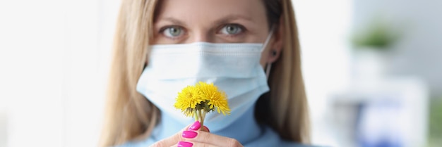 Vrouw met beschermend medisch masker die gele bloemen snuift