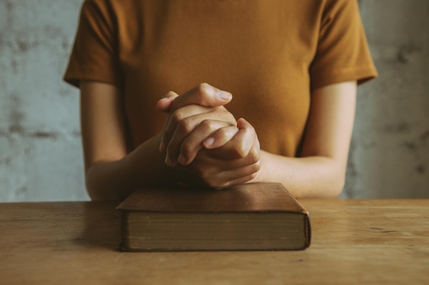 Foto vrouw met bijbel biddende handen samengevoegd op haar bijbel op houten tafel