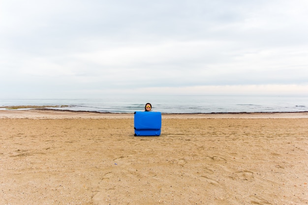 Vrouw met blauwe koffer op het strand. Grappig beeld, grap en humor concept.