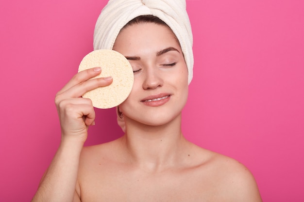 Vrouw met blote schouders, met spons voor het aanbrengen van make-up foundation, vrouwelijke staande in bathroomwith