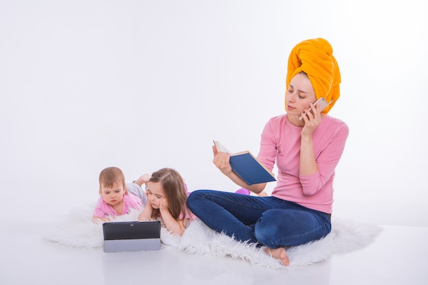 Vrouw met boek in haar handen praat over de telefoon. Kinderen kijken cartoon op hun tablet. moeder waste haar haar. handdoek op het hoofd. Hobby's en recreatie met gadgets.