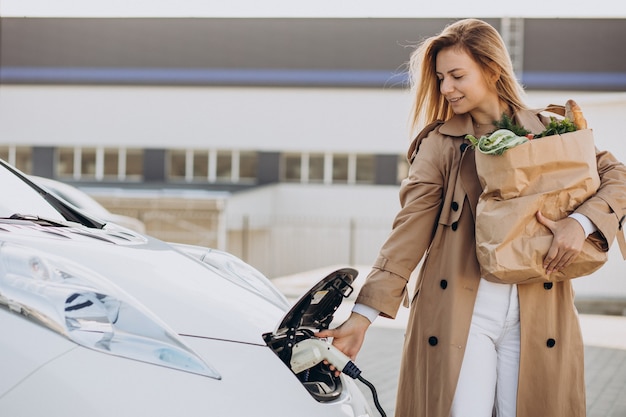 Vrouw met boodschappentassen die elektrische auto oplaadt