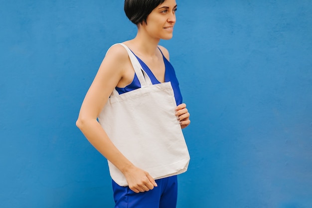 Vrouw met canvas draagtas op heldere blauwe achtergrond in de stad. Herbruikbare eco-tas. Milieuvriendelijk concept.