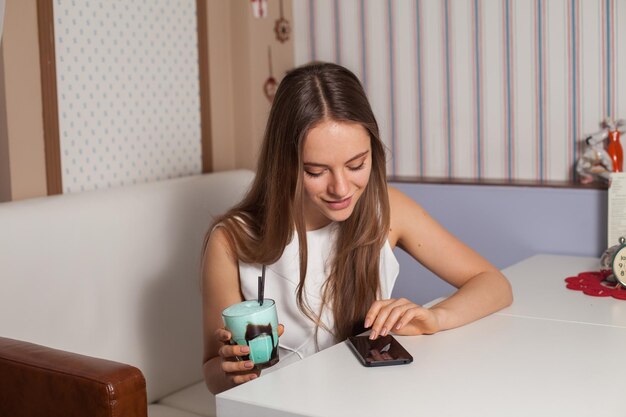 Vrouw met cocktail en mobiel in café