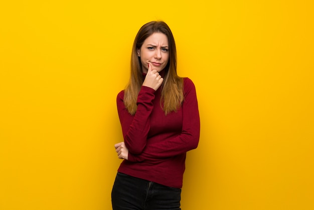 Vrouw met coltrui over gele muur denken