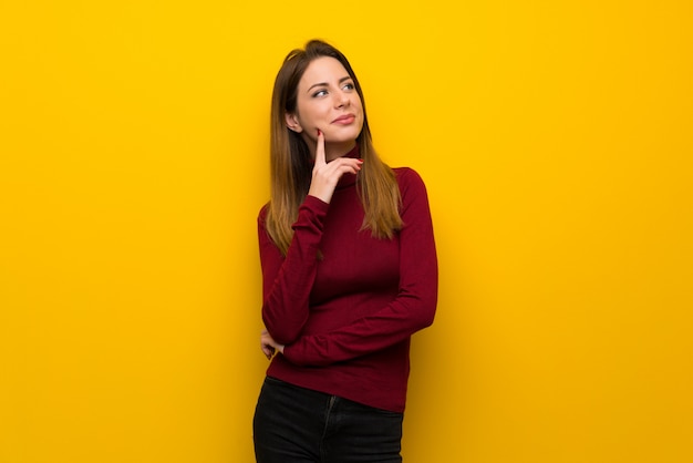 Vrouw met coltrui over gele muur die een idee denken terwijl omhoog het kijken