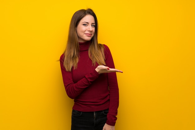 Vrouw met coltrui over gele muur die een idee voorstelt terwijl het kijken naar het glimlachen