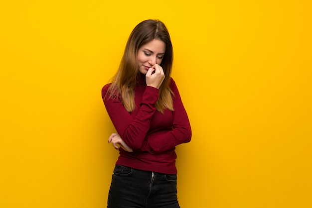 Vrouw met coltrui over gele muur die twijfels hebben