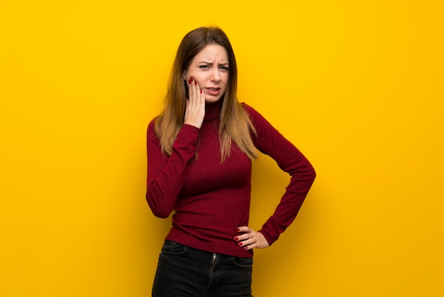 Vrouw met coltrui over gele muur met tandpijn