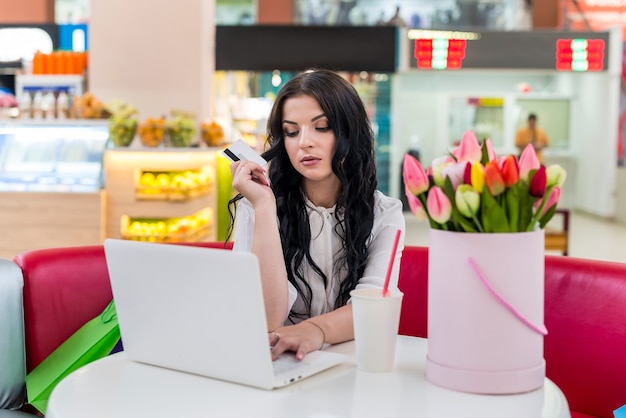 Vrouw met creditcard en laptop in café winkelen