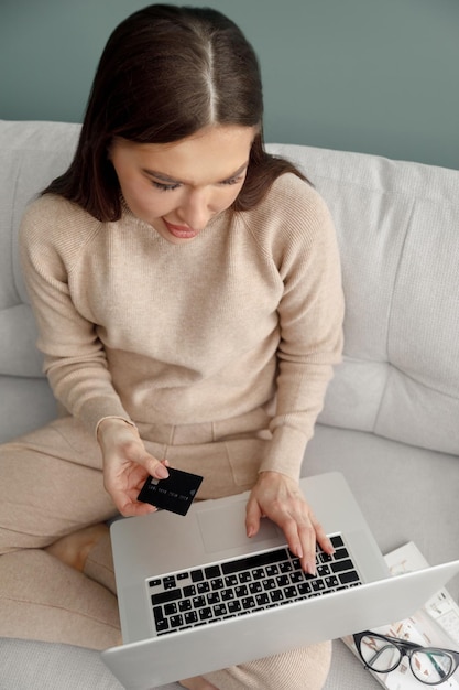 Vrouw met creditcard en met behulp van laptopcomputer zittend op de bank thuis online winkelen concept