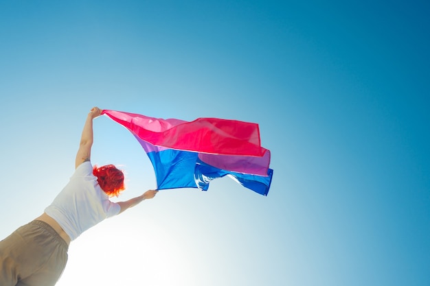 Vrouw met de biseksuele regenboogvlag met de blauwe lucht op de achtergrond