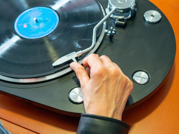 Foto vrouw met de hand die de toonarm van haar draaitafel vasthoudt, klaar om een vinylplaat af te spelen