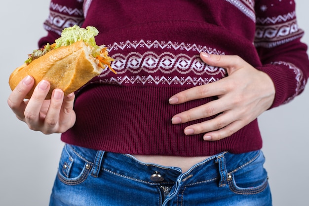 Vrouw met de helft van de sandwich in de ene hand en een andere hand op volle maag