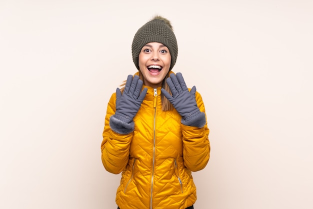 Vrouw met de winterhoed over geïsoleerde muur met verrassingsgelaatsuitdrukking