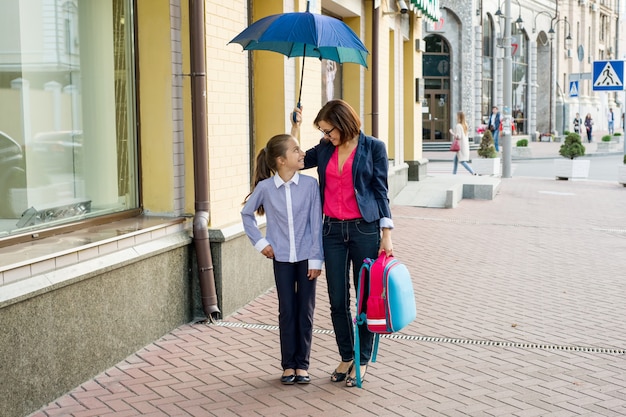 Vrouw met dochter die samen naar school onder een paraplu loopt.