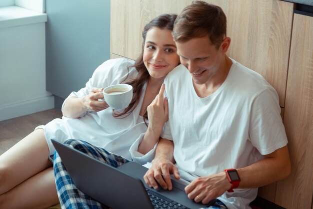 Vrouw met donkere ogen die koffie drinkt terwijl echtgenoot aan laptop werkt