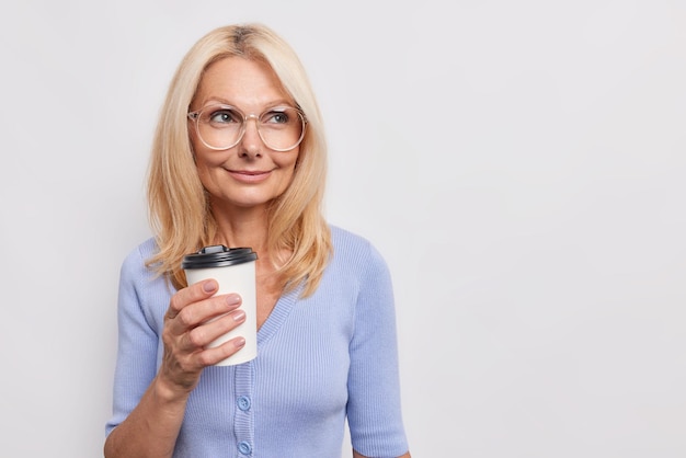vrouw met dromerige uitdrukking drinkt afhaalmaaltijden koffie geniet van aromatische drank draagt transparante bril blauwe trui geïsoleerd op wit kopie ruimte