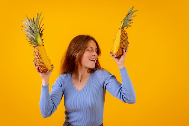 Vrouw met een ananas in een zonnebril die danst en blij is met de ananas die op een halve gele achtergrond is gesneden