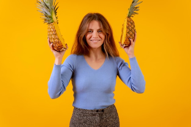 Vrouw met een ananas in zonnebril lachend met ananas gesneden in halve gele achtergrond