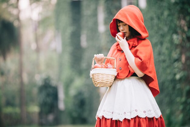 Vrouw met een appel en een mand terwijl ze tegen bomen staat