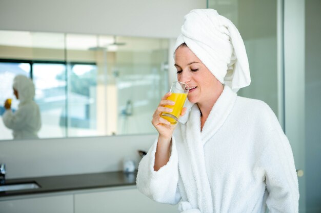 vrouw met een badjas en een handdoek op haar hoofd drinkt een glas sinaasappelsap