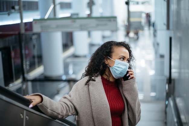 Vrouw met een beschermend masker die op een smartphone praat op de trappen van een metroroltrap