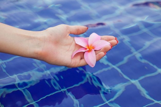 Vrouw met een bloem van plumeria door handen over water