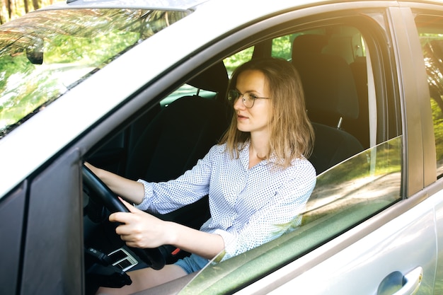 Vrouw met een bril bestuurt een auto. Meisje achter het stuur.