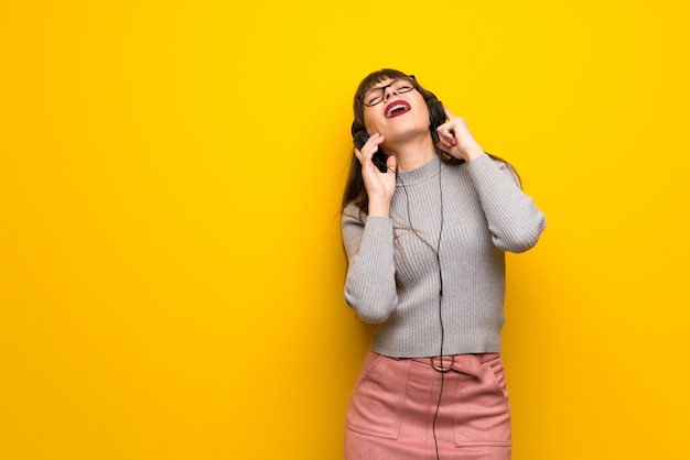 Vrouw met een bril over gele muur luisteren naar muziek met een koptelefoon