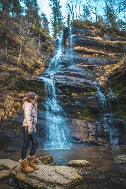 vrouw met een bruine jas en een hoed naast een waterval