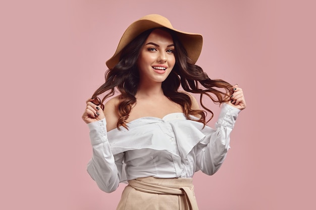 Vrouw met een charmante glimlach met haar donkerbruine haar in een beige hoed en een wit overhemd