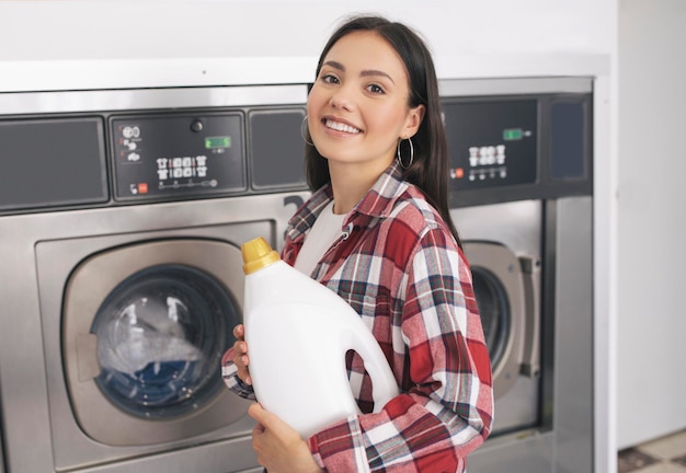 Vrouw met een detergentfles bij wasmachines bij de wasserette