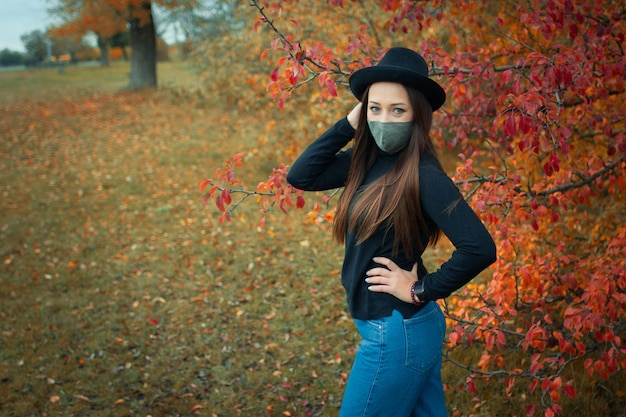vrouw met een doek masker en hoed poseren in herfst park
